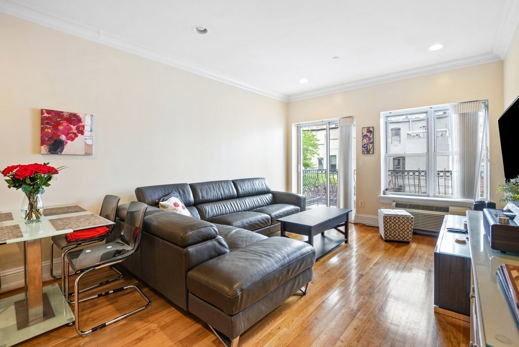 Furnished living room with a dark leather sectional, hardwood floors, and large balcony windows.
