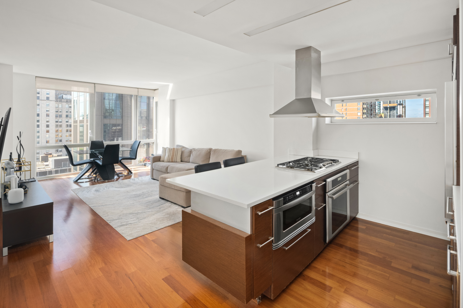 Open-plan kitchen and living area with a large island, hardwood floors, and city views through tall windows.