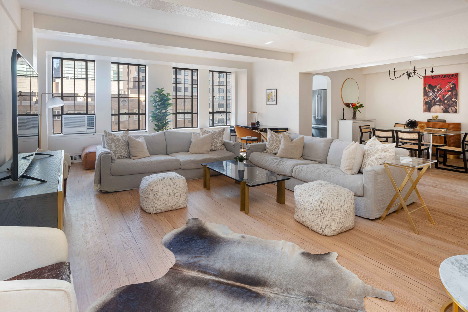 Open-plan living and dining room with a gray sectional, hardwood floors, and tall black-framed windows.