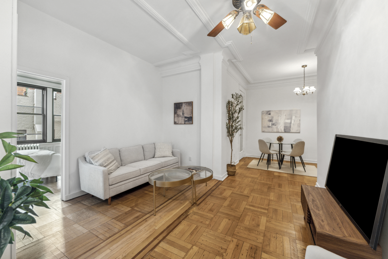 Staged living room and dining area with parquet floors, a gray sofa, and ornate crown molding.