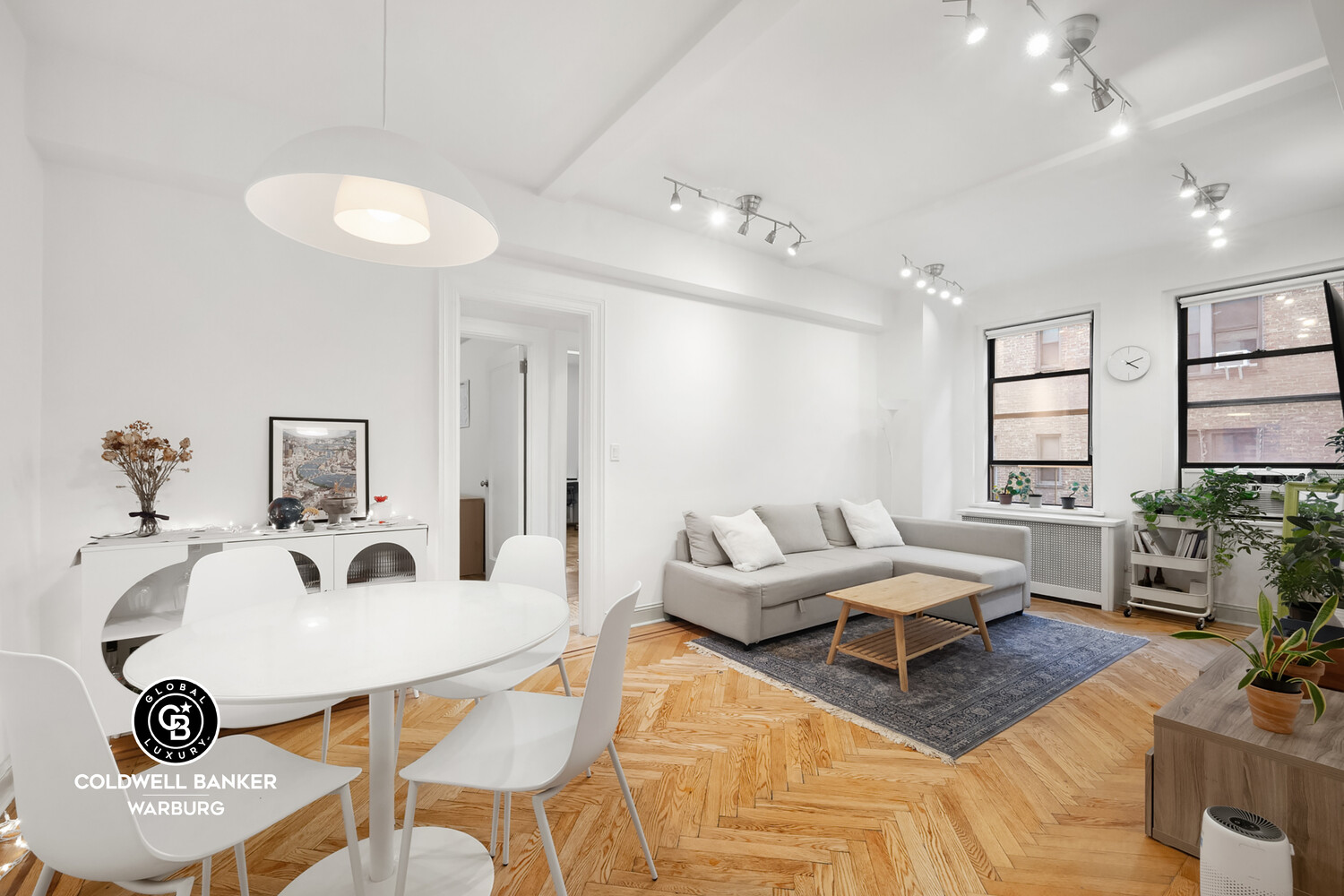 Bright apartment living and dining area with a gray sectional and herringbone wood floors.