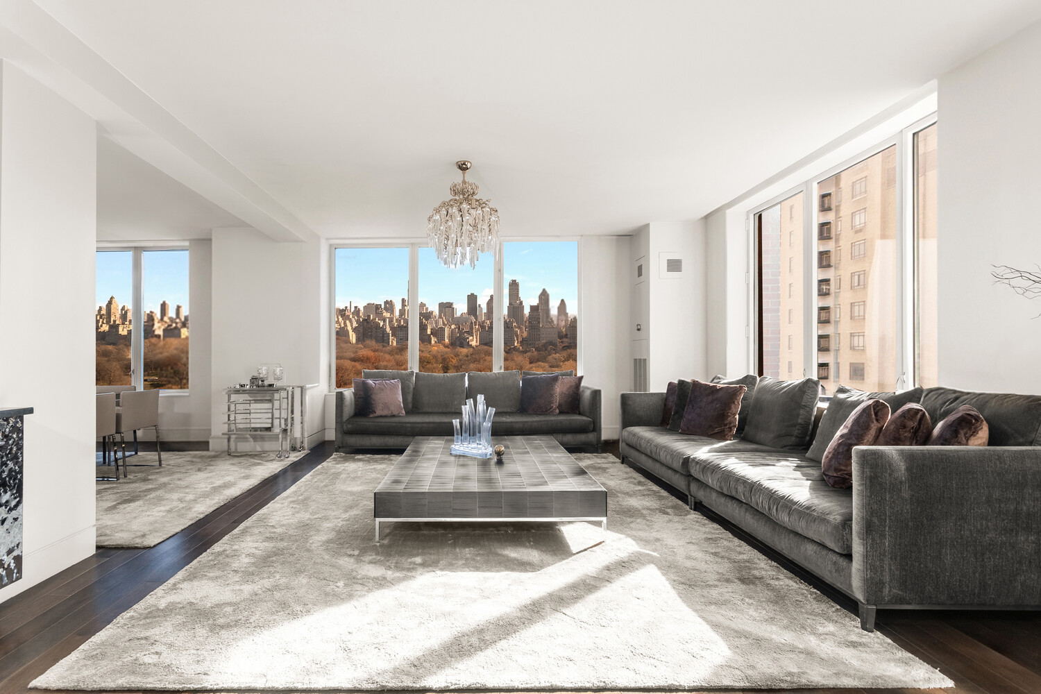 Living room with gray sofas and panoramic windows overlooking Central Park and the Manhattan skyline.