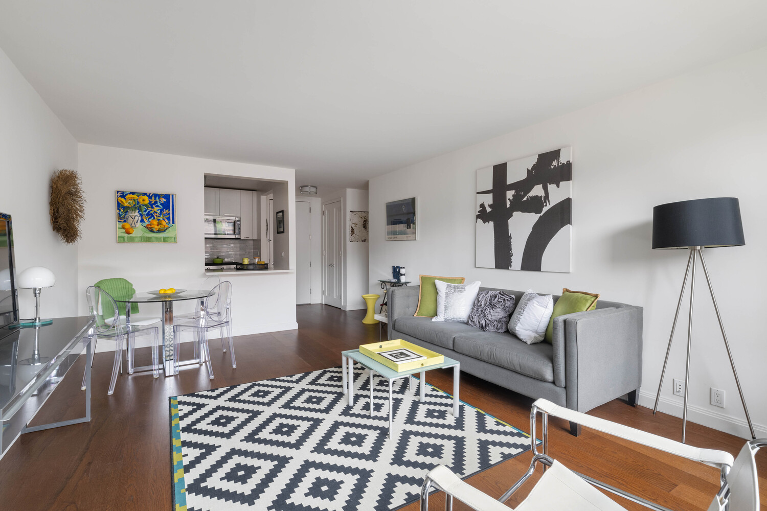 Open-plan living and dining area with a gray sofa, geometric rug, and glass dining table.
