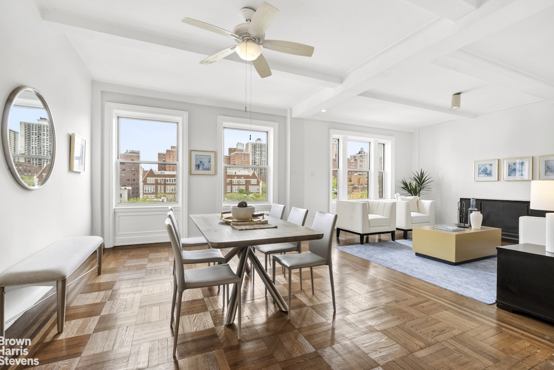 Bright apartment living and dining room with parquet floors and large windows overlooking city buildings.