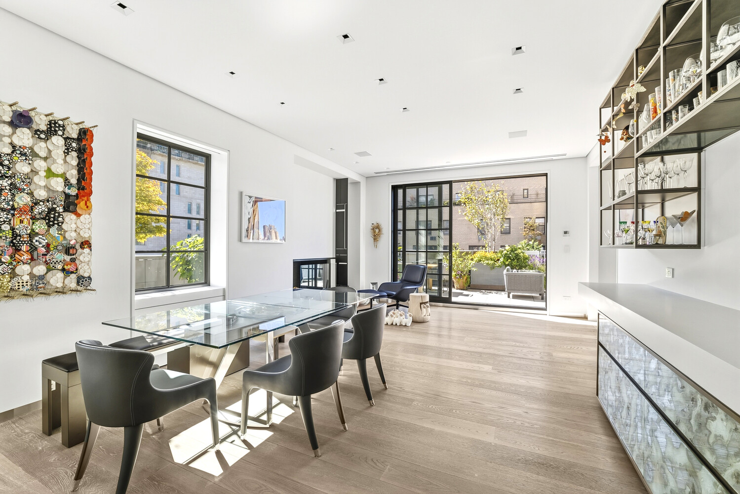 Modern dining area with a glass table, dark chairs, and large windows overlooking a planted terrace.