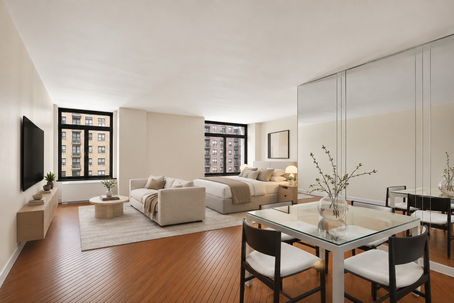 Open-plan apartment bedroom and dining area with large windows and warm wood floors.