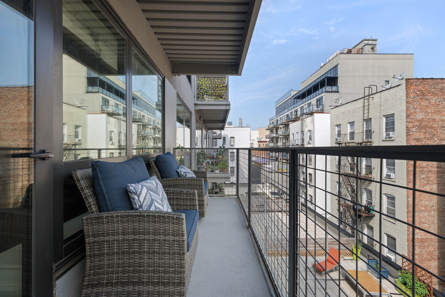 Furnished apartment balcony with a blue-cushioned sofa and views of neighboring city buildings.