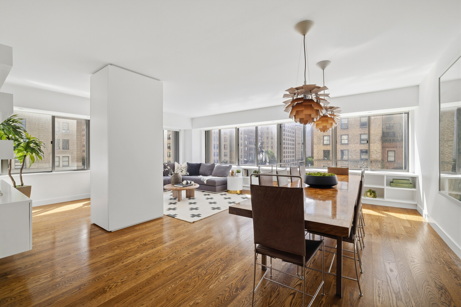 Bright open-plan apartment with polished hardwood floors, a gray sectional, and wide city-facing windows.