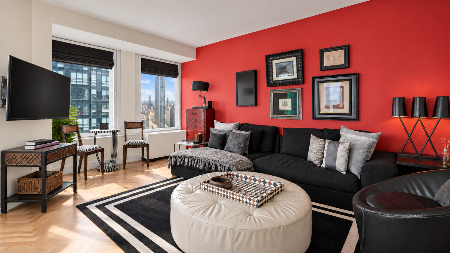 Living room with a red accent wall, black sectional sofa, and city views through large windows.