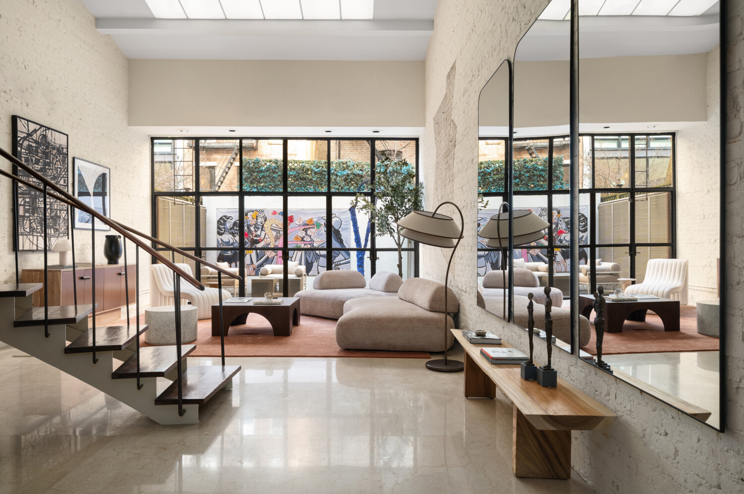 Contemporary living room with a sculptural sectional, white brick walls, and large windows overlooking a colorful mural.