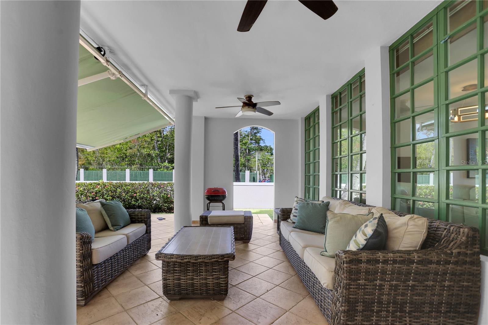 Covered patio with wicker seating, green-framed windows, and tiled flooring.