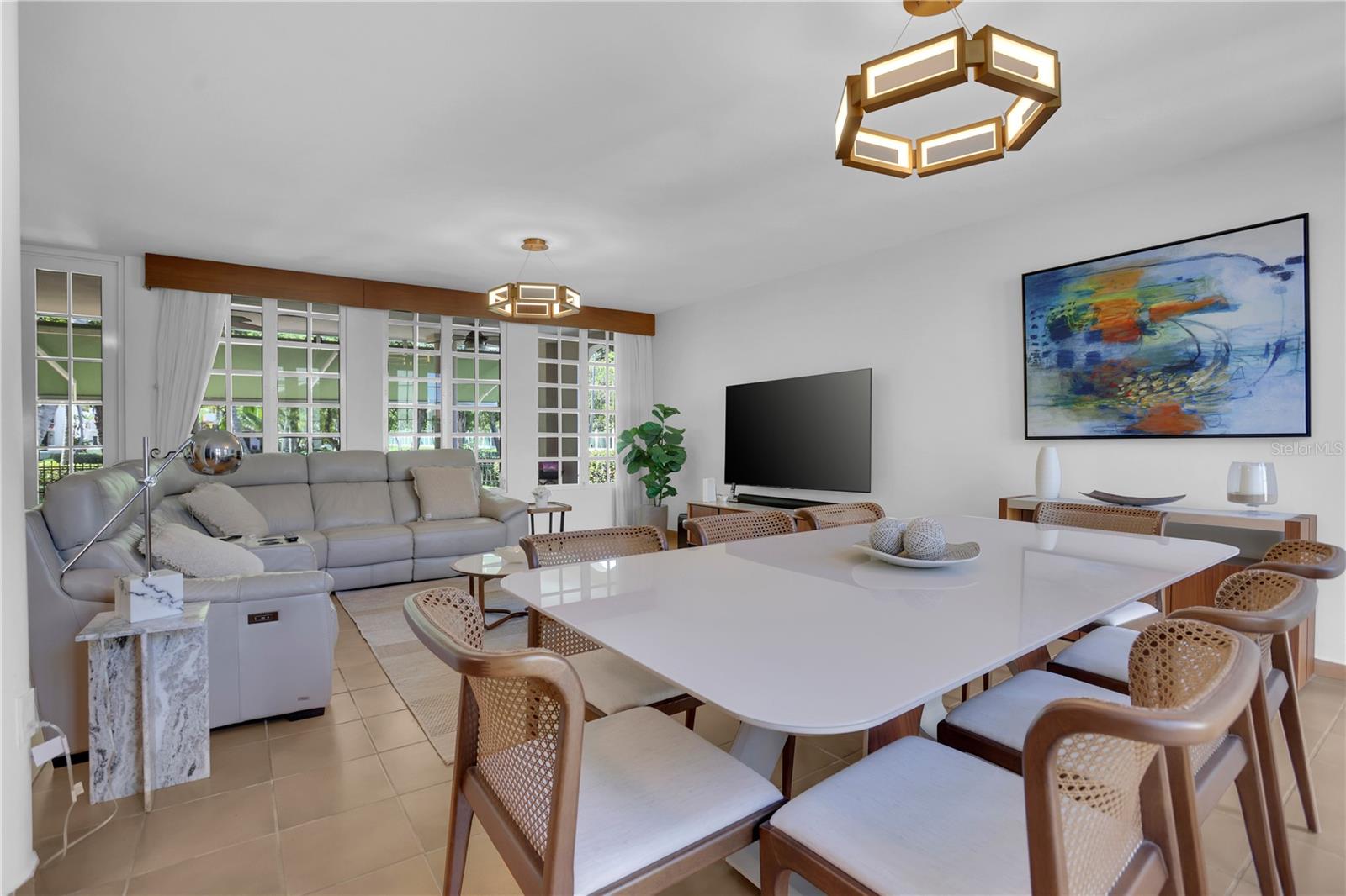 Living and dining area with a large white table, gray sectional, and tall grid-pane windows.