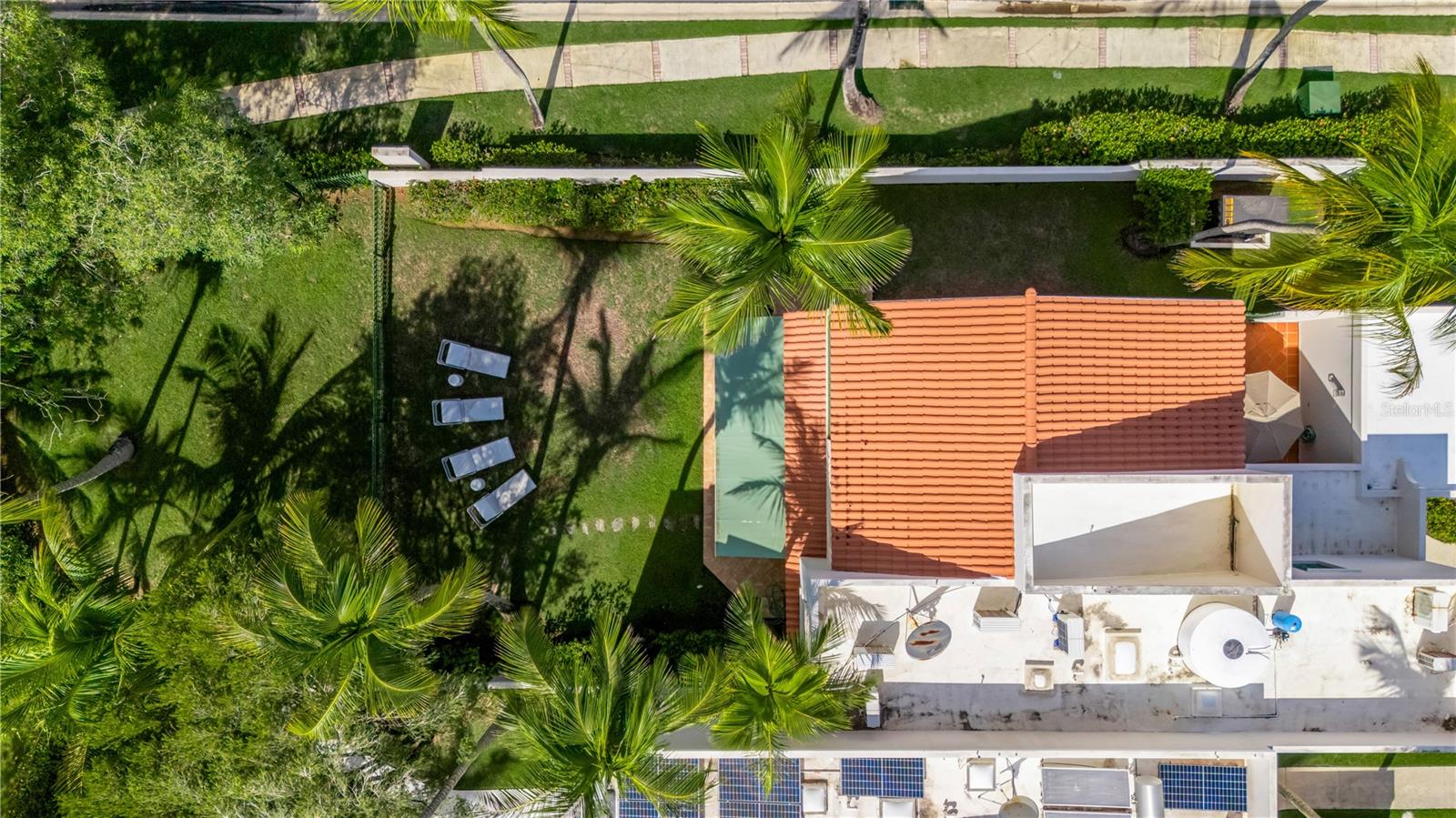 Aerial view of a tile-roofed home, palm-lined lawn, and rooftop solar panels.