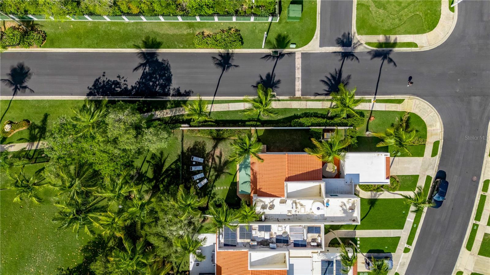 Aerial view of a white home with terracotta roof sections, solar panels, and palm-filled landscaping.