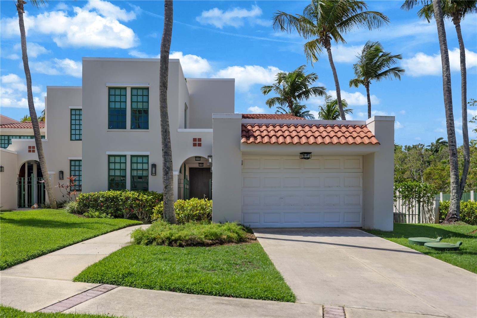 Modern white two-story home with a red tile garage roof, landscaped lawn, and tall palm trees.