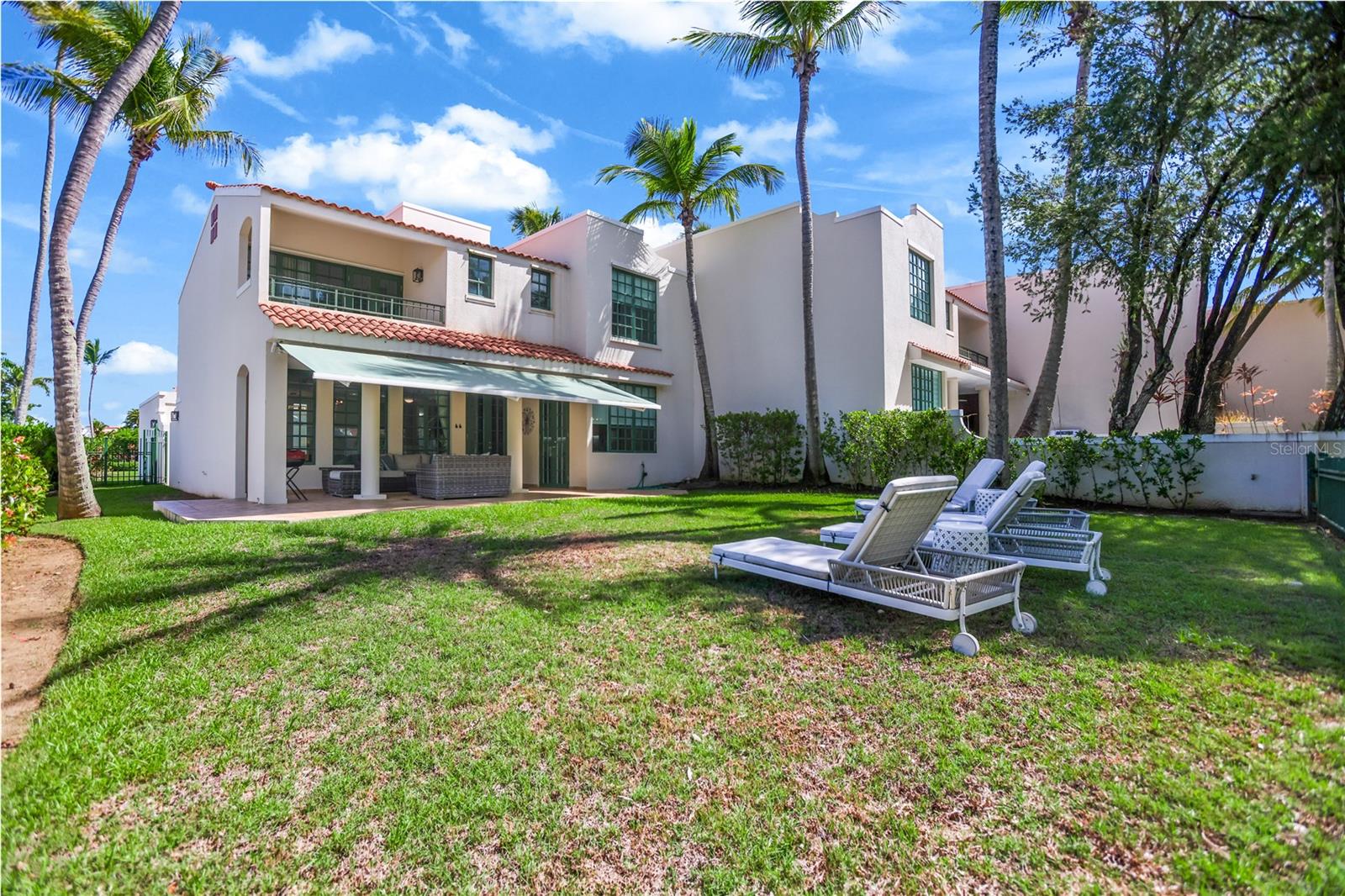 Two-story white home with a covered patio, palm-lined lawn, and reclining lounge chairs.