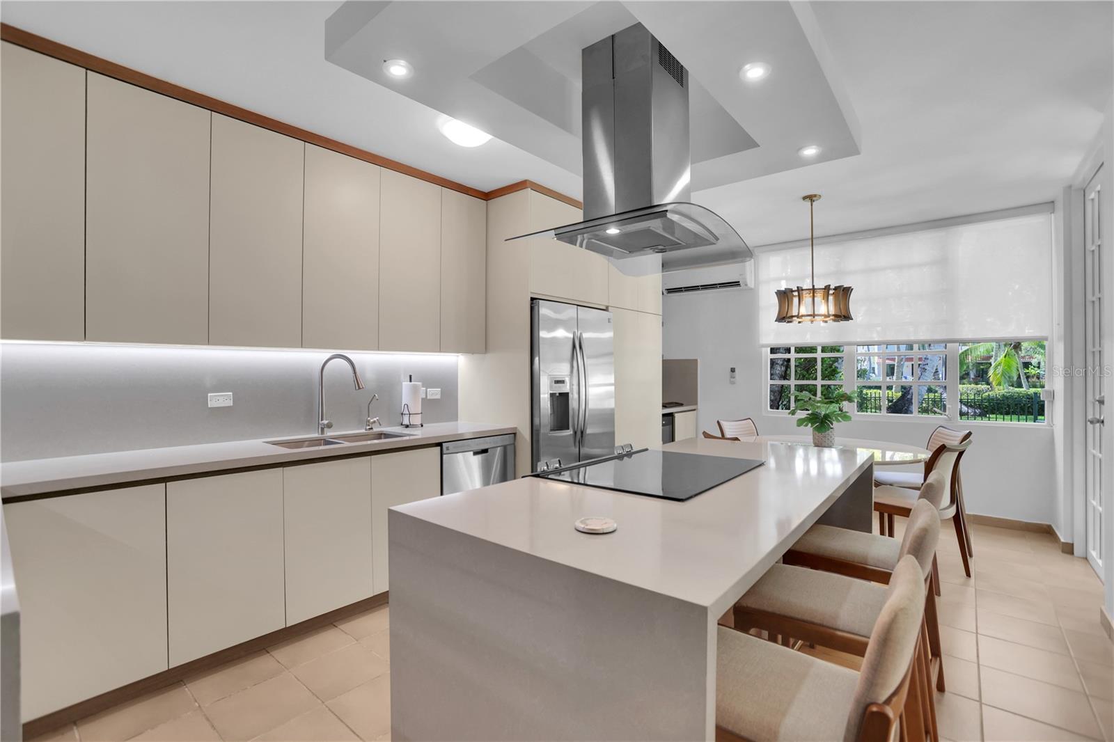 Modern kitchen with a large island, black cooktop, stainless steel appliances, and adjoining dining area.