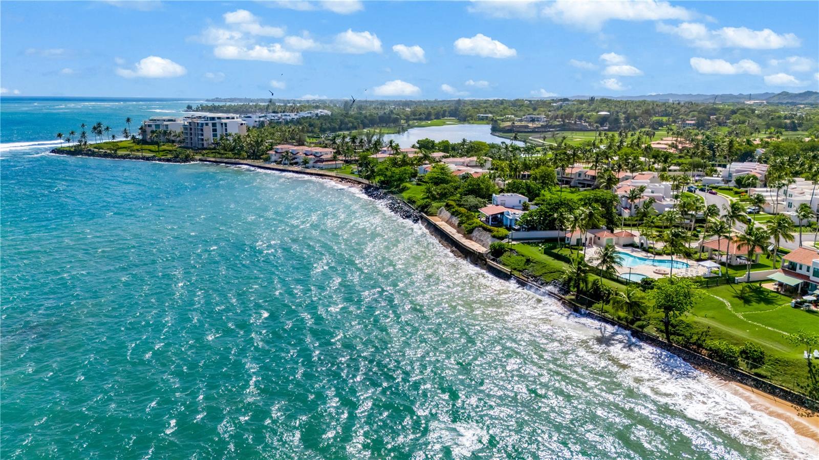 Aerial view of a coastal neighborhood with turquoise water, palm-lined homes, and a golf course.