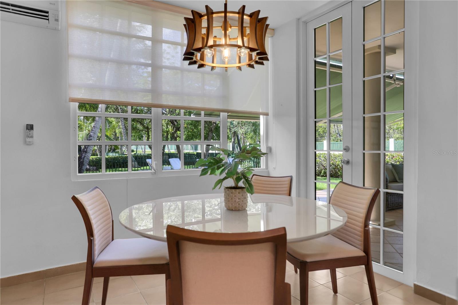 Dining area with a round glass table, sculptural pendant light, and garden views through large windows.