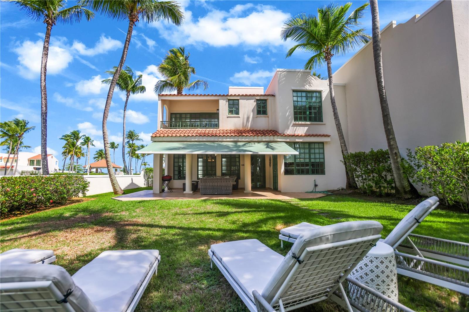 Two-story white home with a covered patio, palm trees, and lounge chairs in the backyard.
