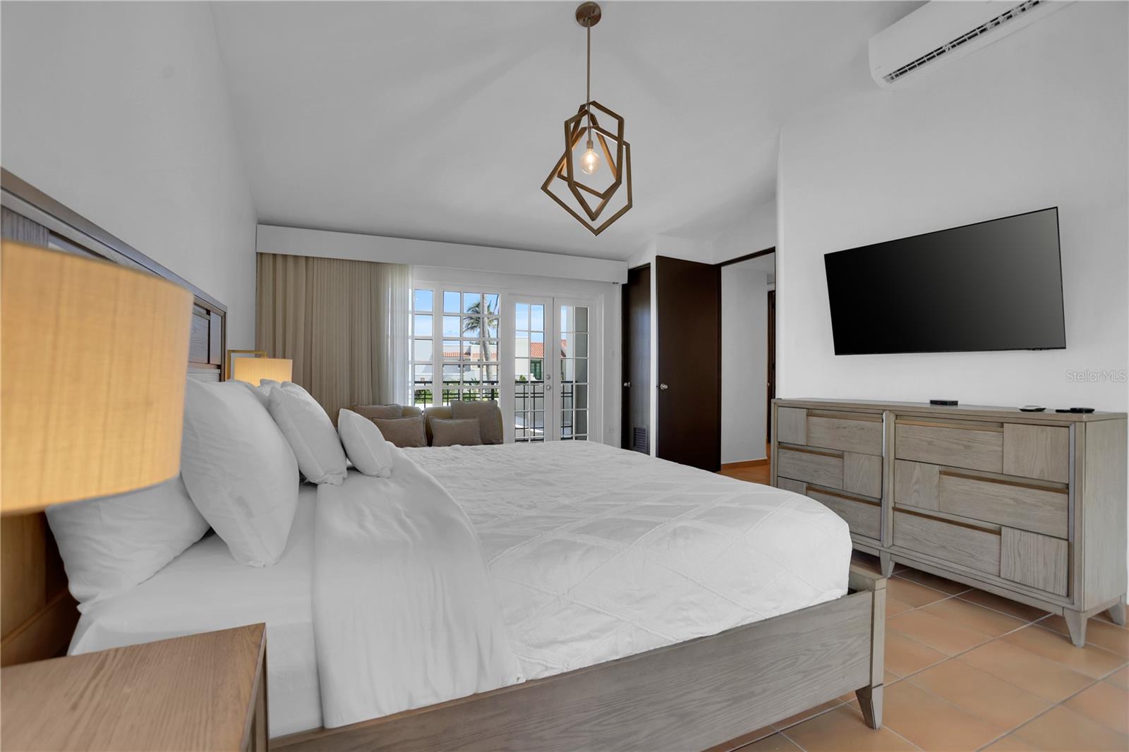 Furnished bedroom with a large white bed, French doors, and a wall-mounted television.
