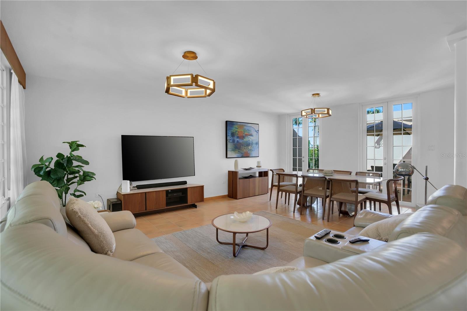 Open-plan living and dining room with cream sofas, wood furnishings, and tall glass doors.