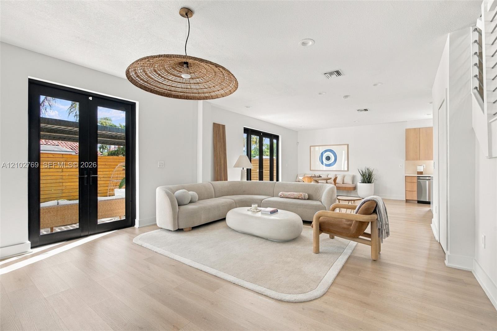 Bright living room with a curved cream sectional, woven pendant, and black-framed patio doors.