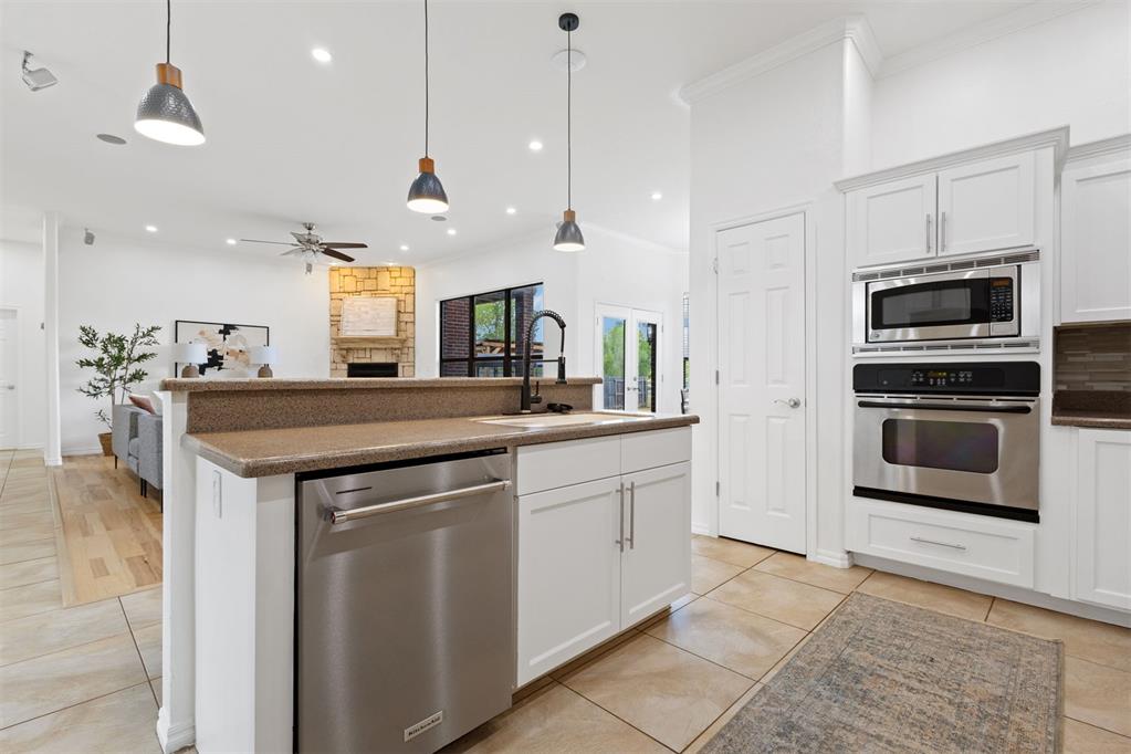 Open-plan kitchen with a granite island, stainless steel appliances, and a stone fireplace visible beyond.