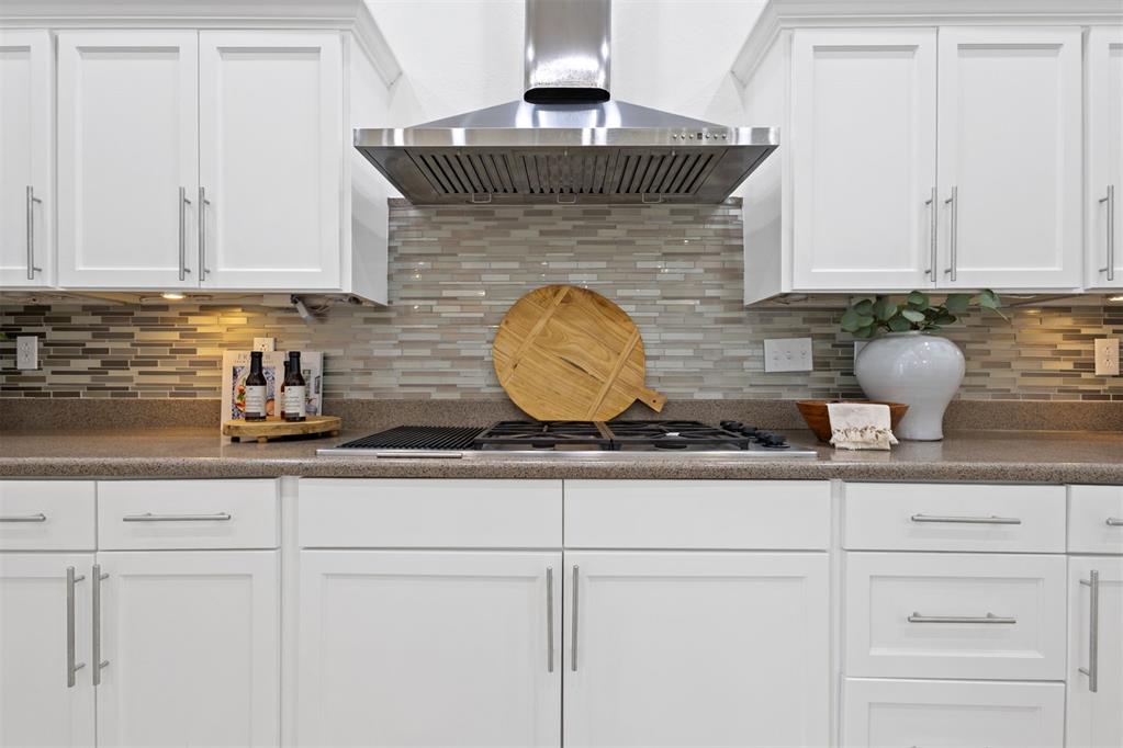 Kitchen range and cooktop beneath a stainless steel hood, with white cabinets and a gray tile backsplash.