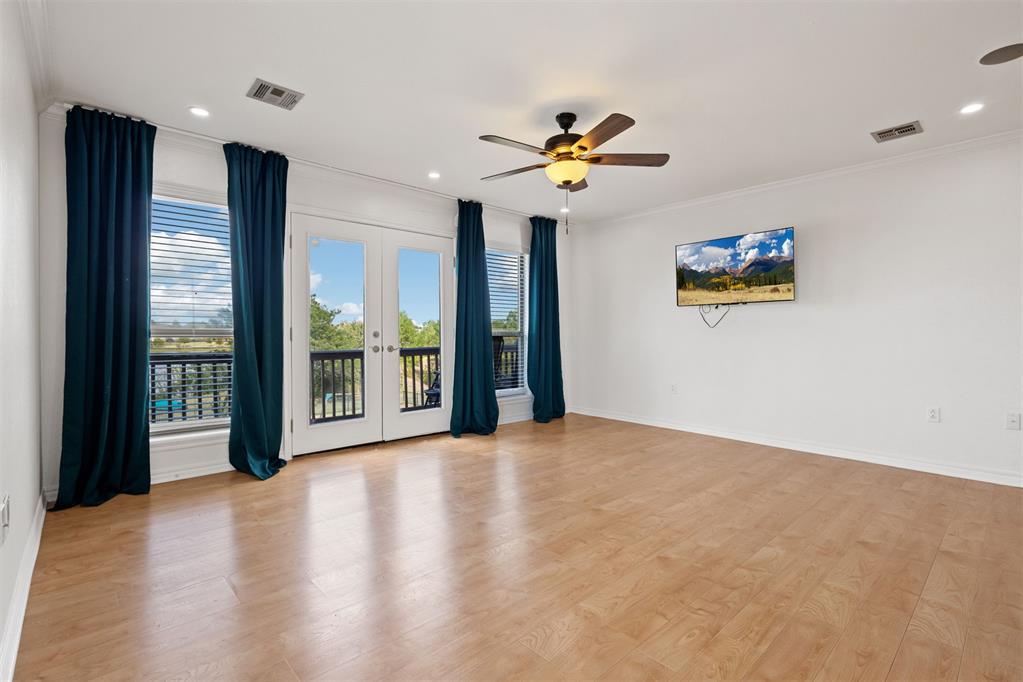 Empty room with light wood floors, teal curtains, and glass doors opening to a balcony.