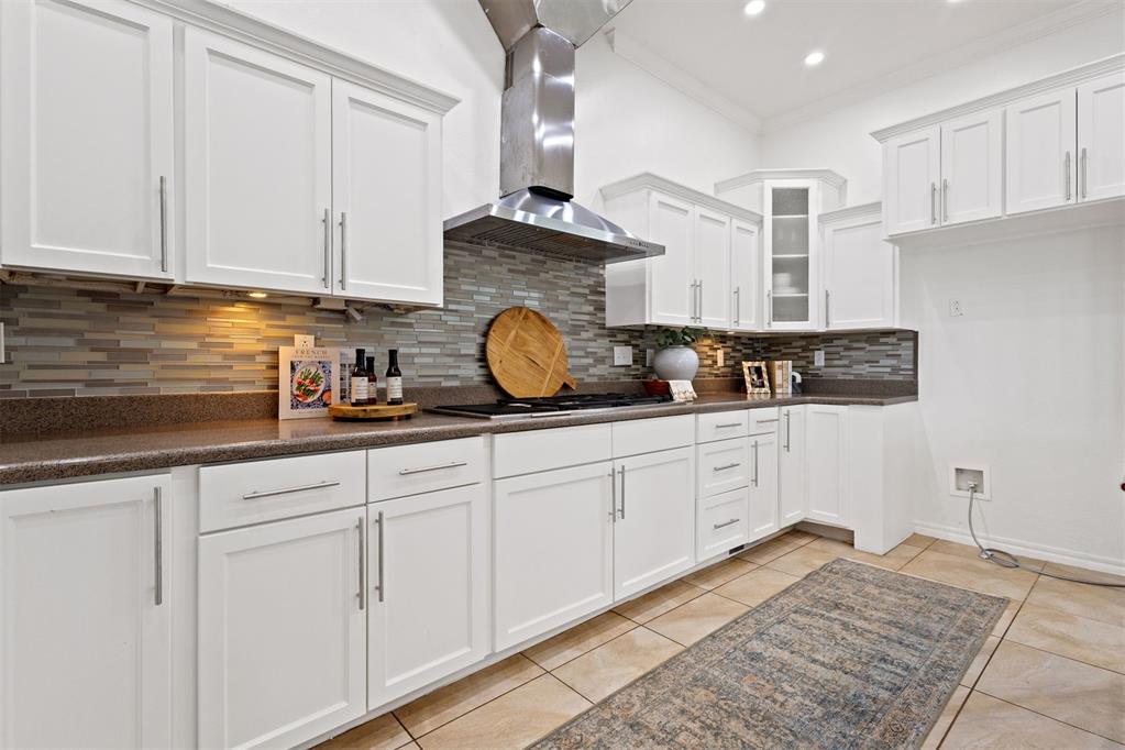 Kitchen with white cabinets, a stainless steel range hood, and multicolored tile backsplash.