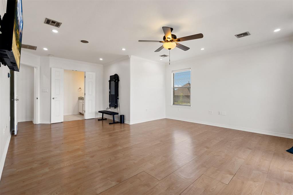 Spacious room with wood floors, a ceiling fan, and exercise equipment beside an open doorway.
