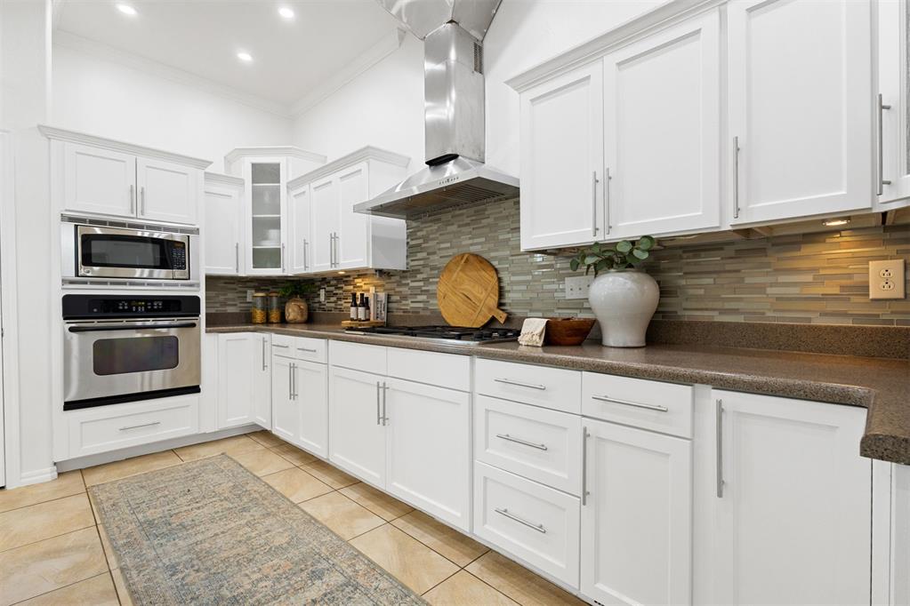 Kitchen with white cabinets, stainless double oven, and multicolored tile backsplash.