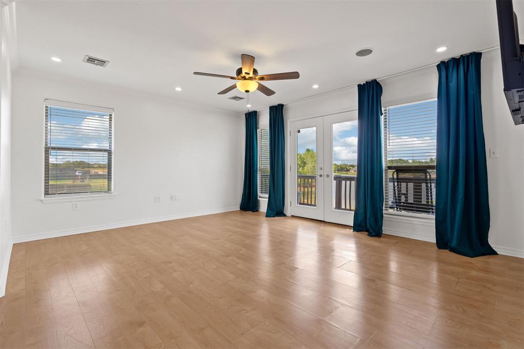 Empty living room with wood-look floors, teal curtains, and French doors opening to a balcony.