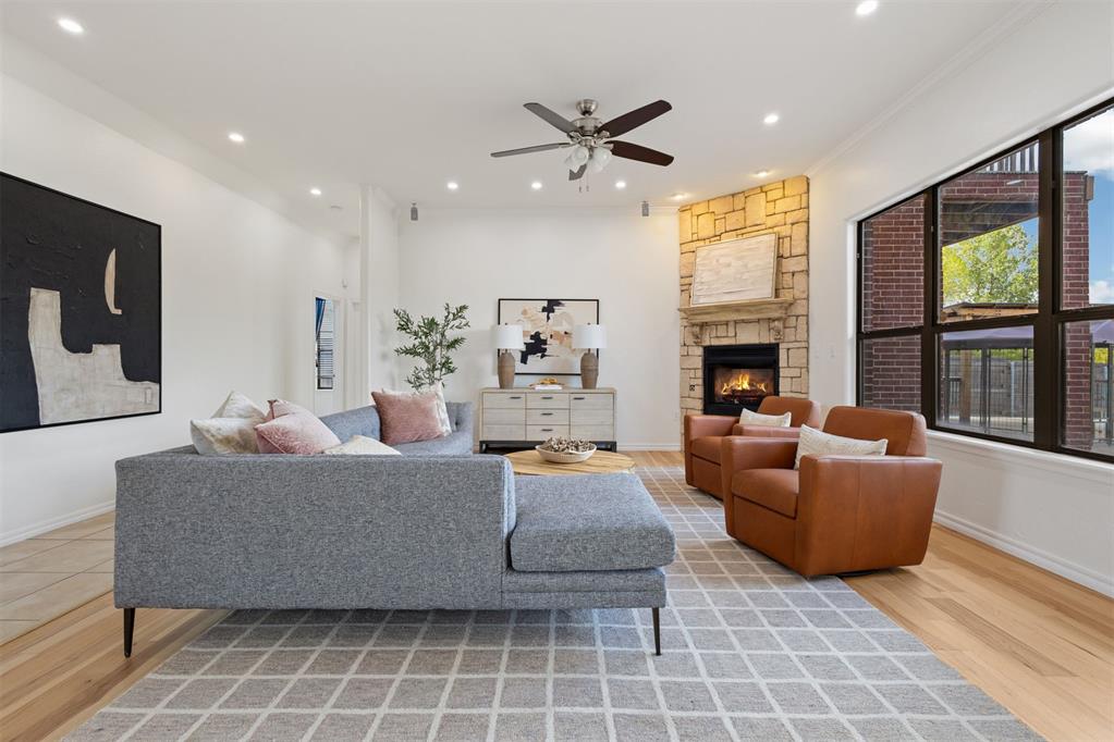 Staged living room with gray sectional, cognac armchairs, and a lit stone fireplace.