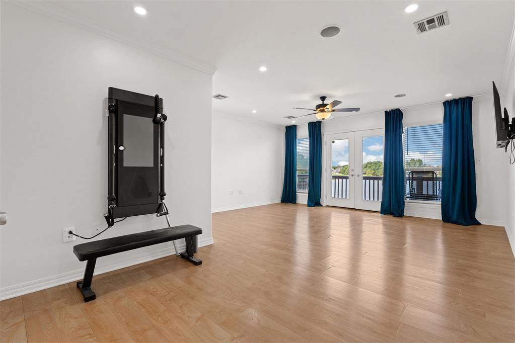 Bright living area with wood flooring, blue curtains, balcony doors, and wall-mounted exercise equipment.