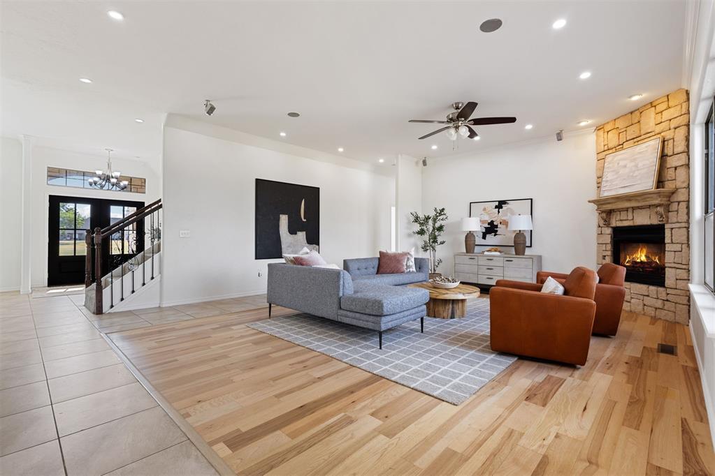 Living room with a gray sectional, rust-colored chairs, hardwood floors, and a stone fireplace.