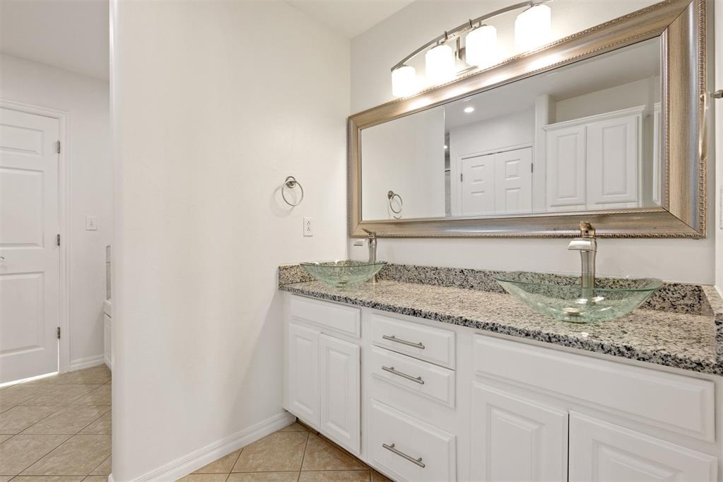 Bathroom vanity with two glass vessel sinks, granite countertop, white cabinets, and a large framed mirror.