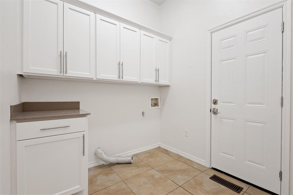 Laundry room with white cabinets, beige tile, a loose dryer vent hose, and an exterior door.