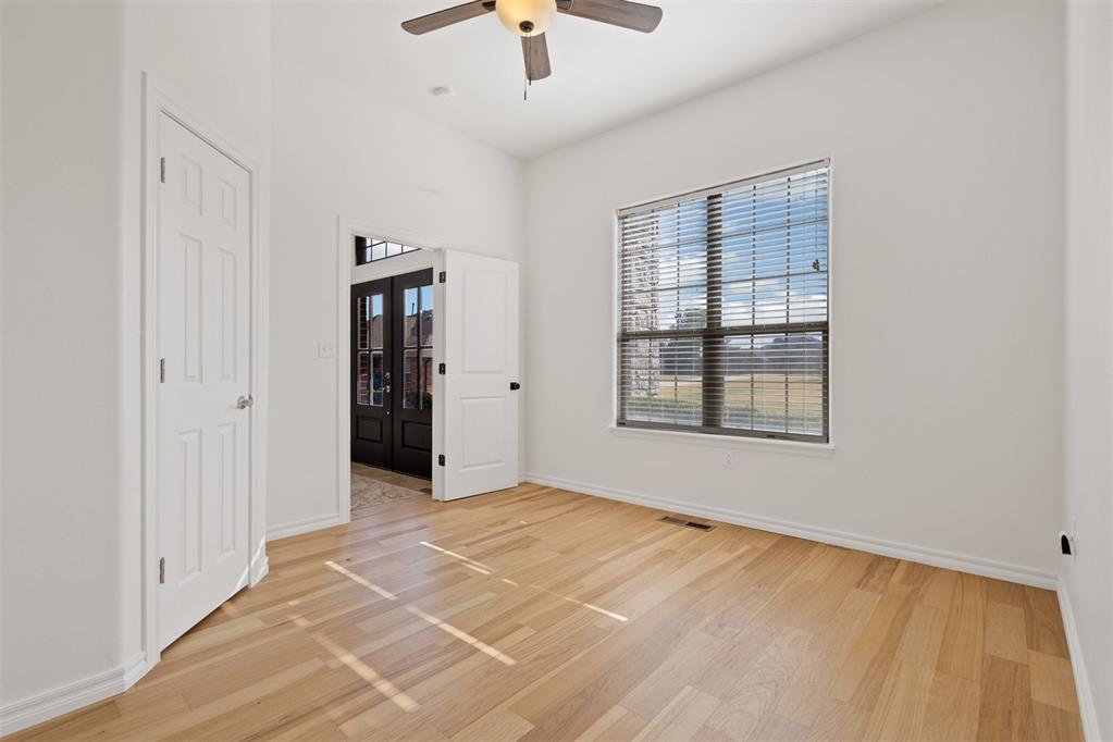 Vacant room with hardwood floors, ceiling fan, and a large window with blinds.