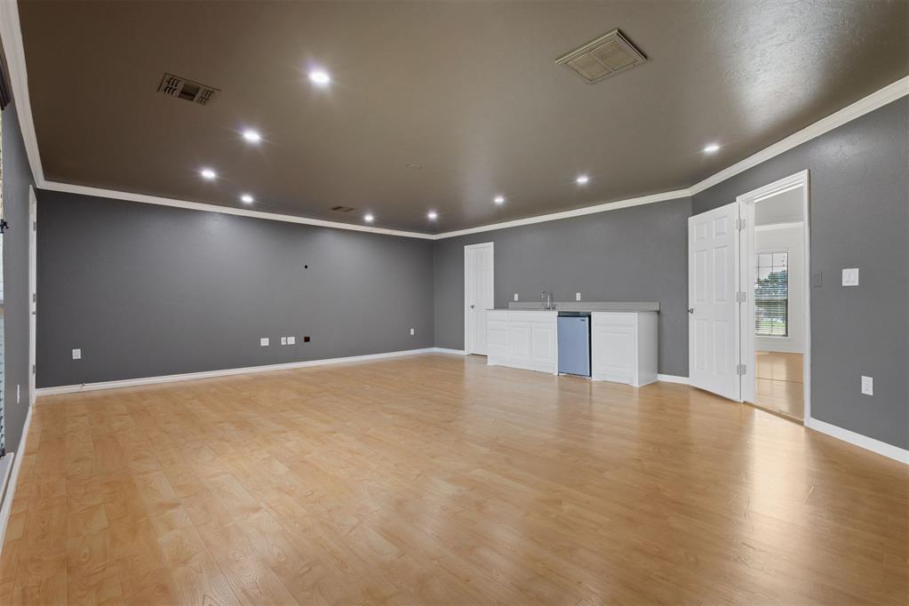 Vacant room with light wood flooring and a kitchenette with white cabinets and a compact refrigerator.