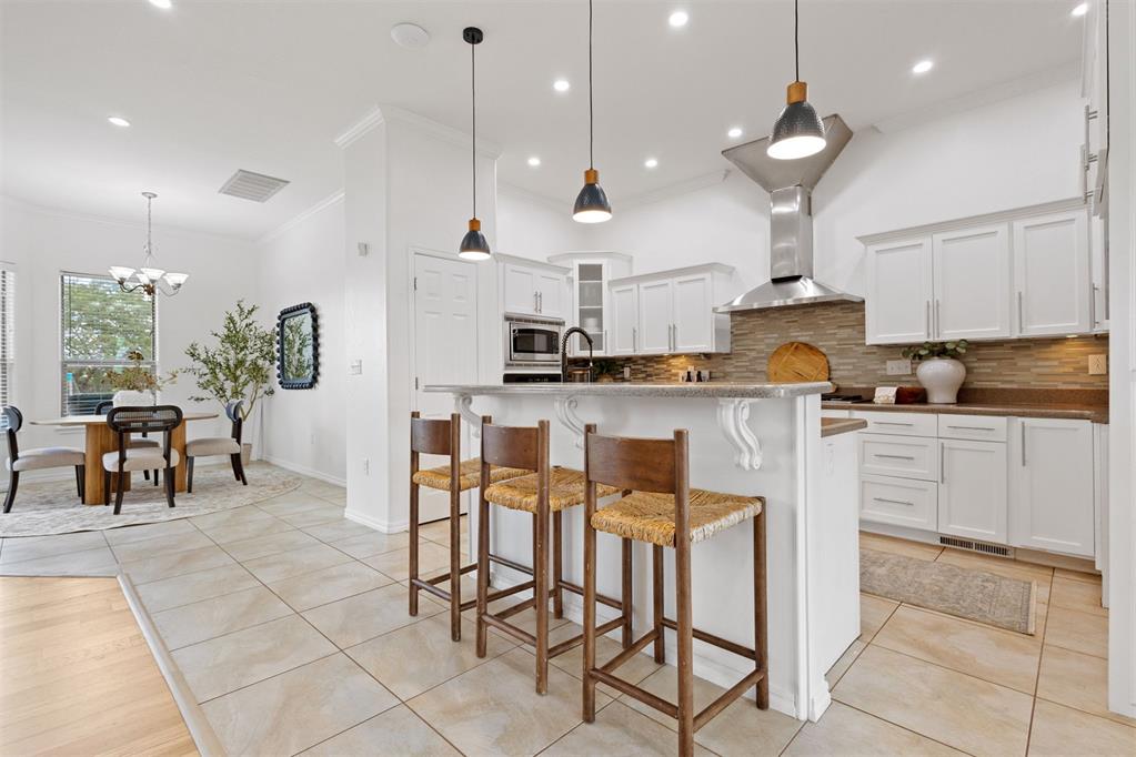 Kitchen with a large island, three wooden stools, white cabinetry, and an adjoining dining area.