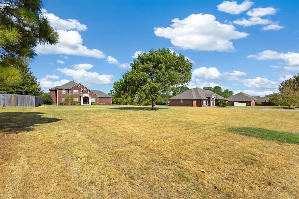 Wide grassy yard with a mature tree and brick homes along the far edge.