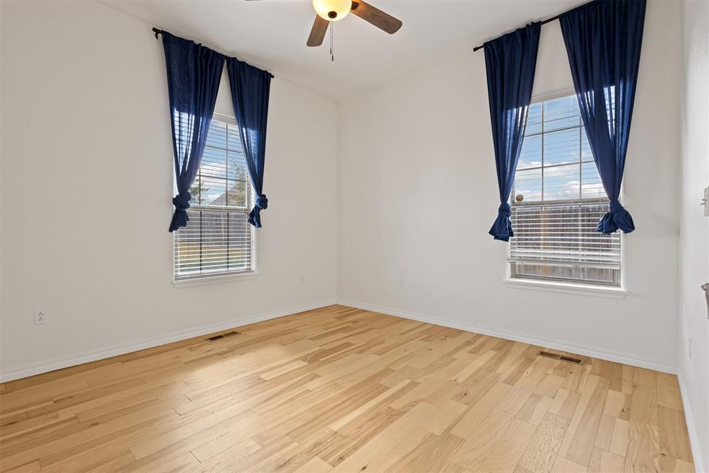 Empty room with light hardwood floors, two curtained windows, and a ceiling fan.