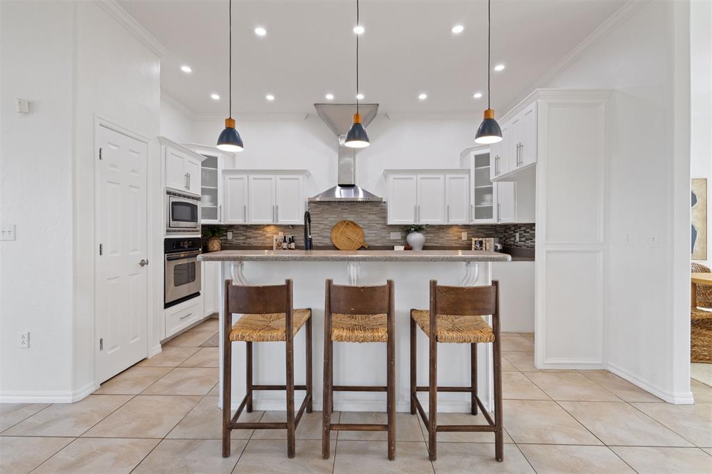 Kitchen with white cabinets, stainless steel appliances, and a large island with three stools.