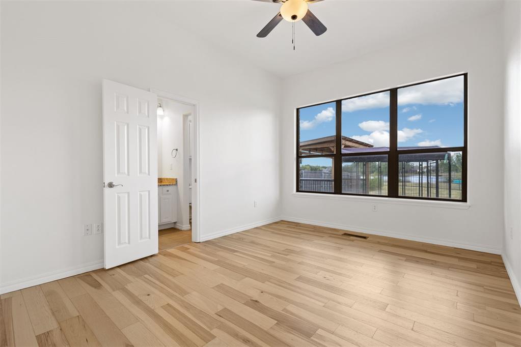 Vacant bedroom with light wood flooring, ceiling fan, and large window.
