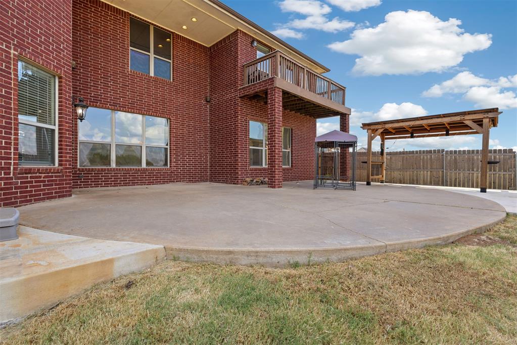 Brick home’s spacious concrete patio with a second-floor balcony and covered pergola.