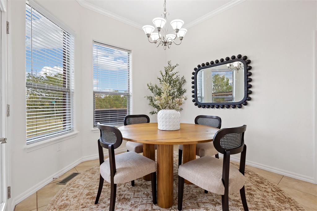 Dining room with a round wooden table, four chairs, and two bright windows.