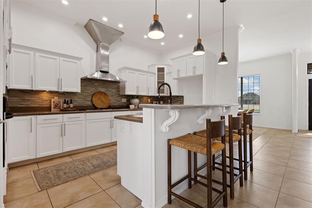 Modern white kitchen with a large island, pendant lights, and three wooden bar stools.