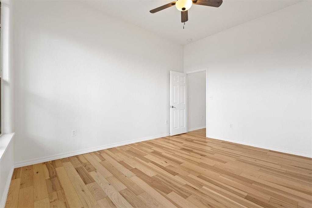 Empty room with light hardwood floors, white walls, a ceiling fan, and an open door.